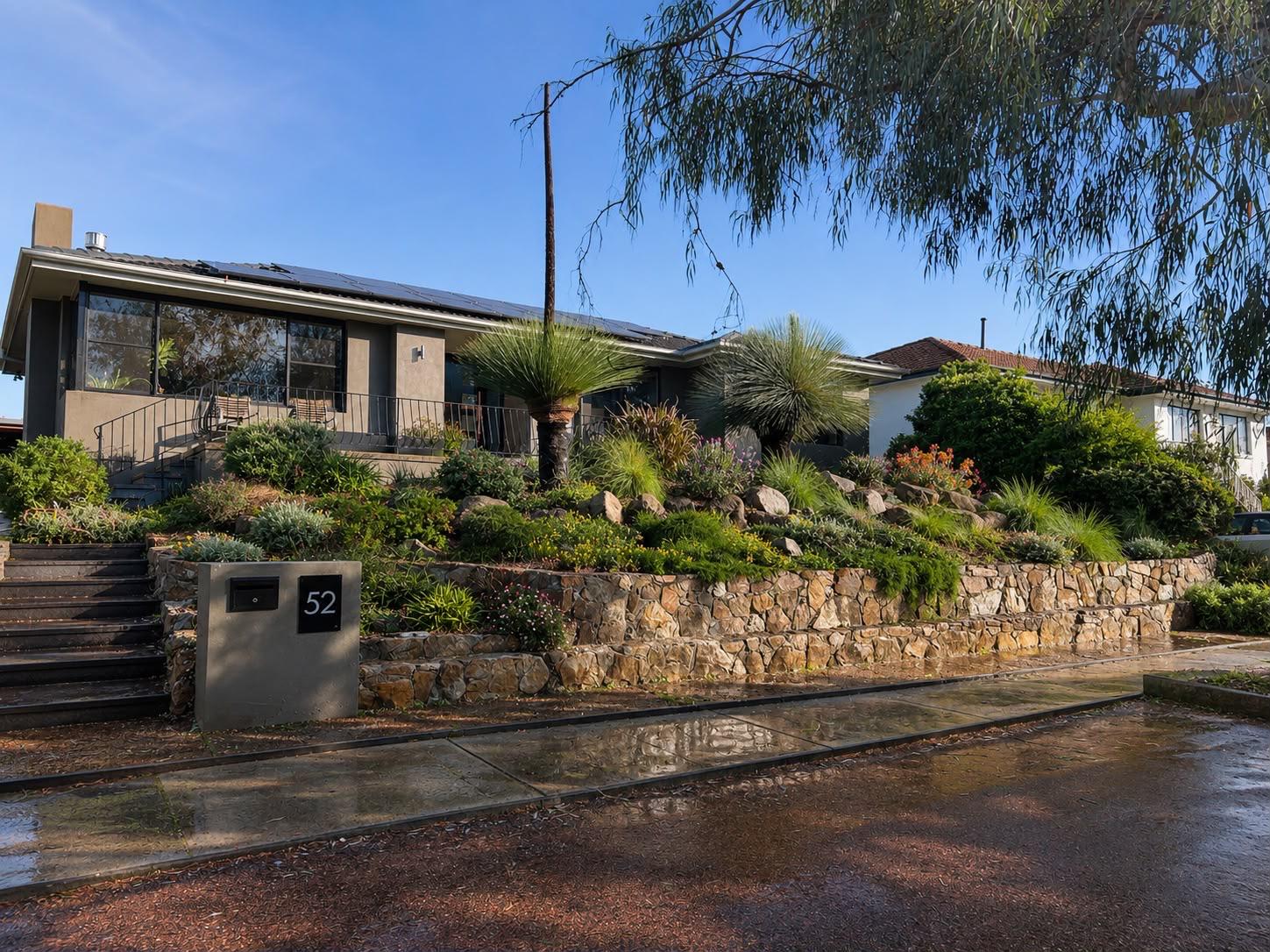 Street view of a home above a natural stone retaining wall planted with natives